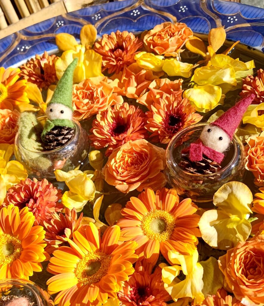 黄色とオレンジの花で埋め尽くされた中に小人のぬいぐるみ
