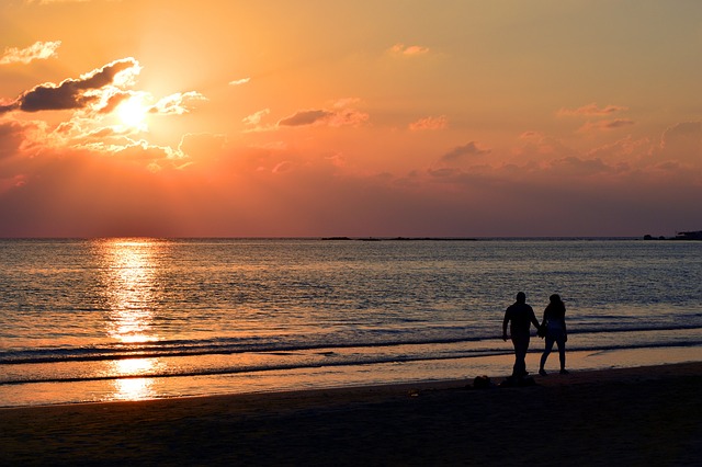 夕日の海辺を手を繋いで歩く男女