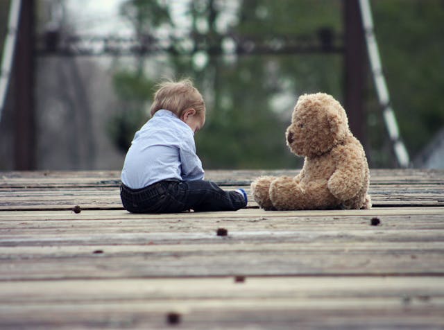熊の大きなぬいぐるみと向かい合って座る小さな子供