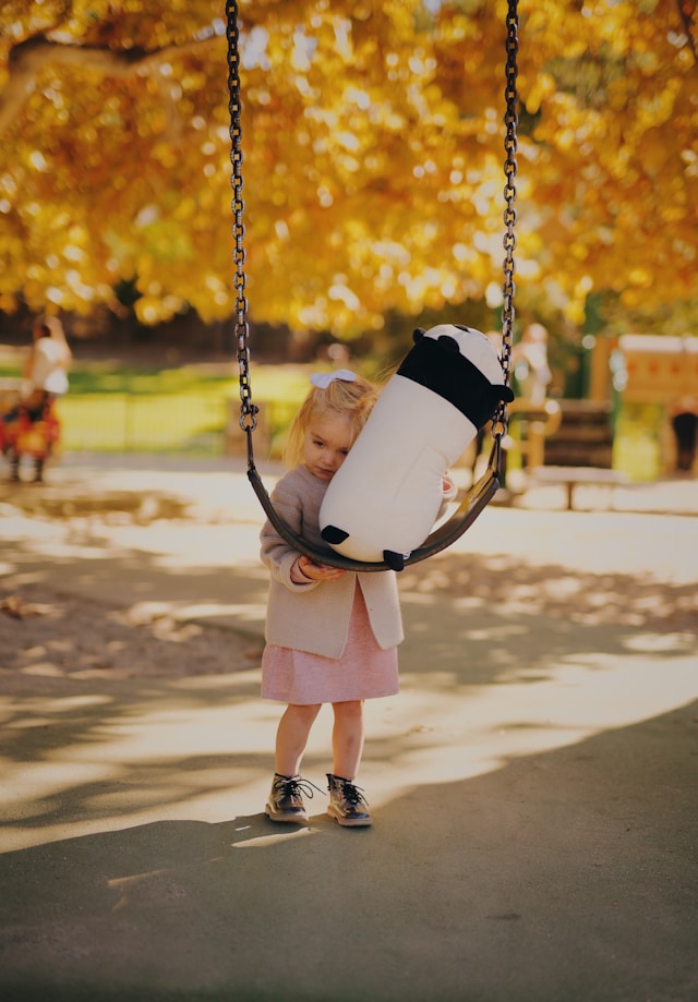 公園のブランコでパンダのぬいぐるみを抱える少女