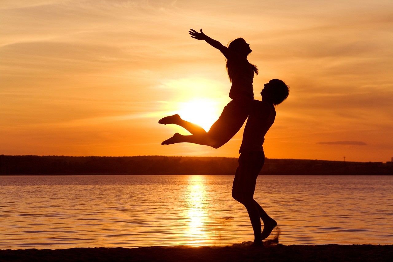 夕日の海辺で彼女を抱える男性